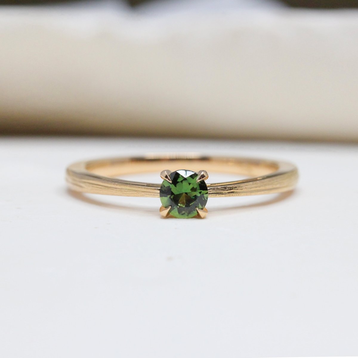 Bague de fiançailles en or rose ornée d'un saphir vert au centre.