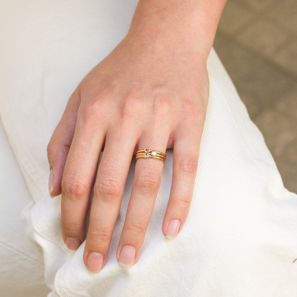 Trois bagues en or portées sur le doigt d'une main, avec des pierres colorées au centre.