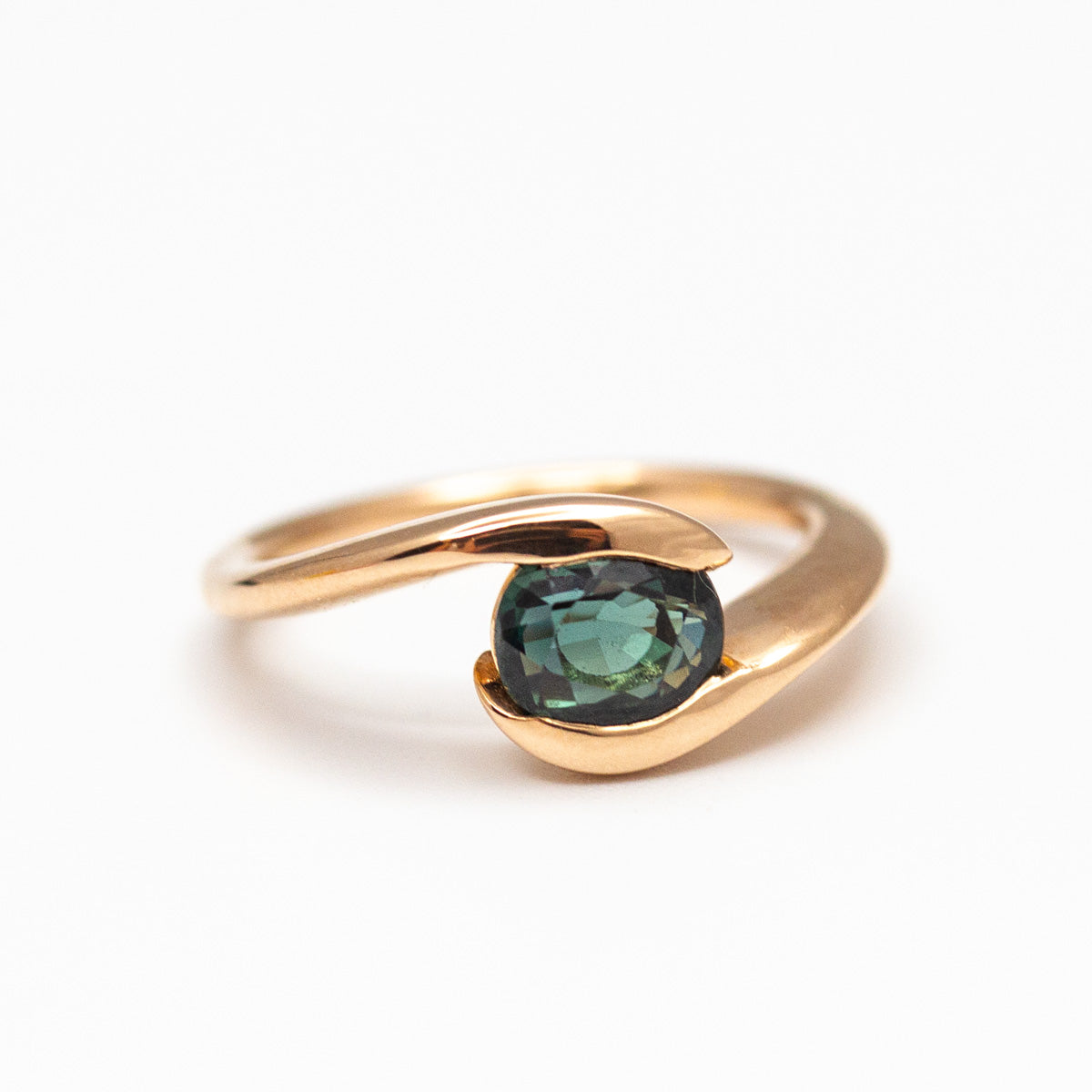 Solitaire sur-mesure avec saphir vert ovale horizontal, entouré d'un anneau asymétrique en or rose-champagne 750/1000 18 carats. Artisan joaillier créateur de bague de fiançailles sur-mesure à Paris et Lyon
