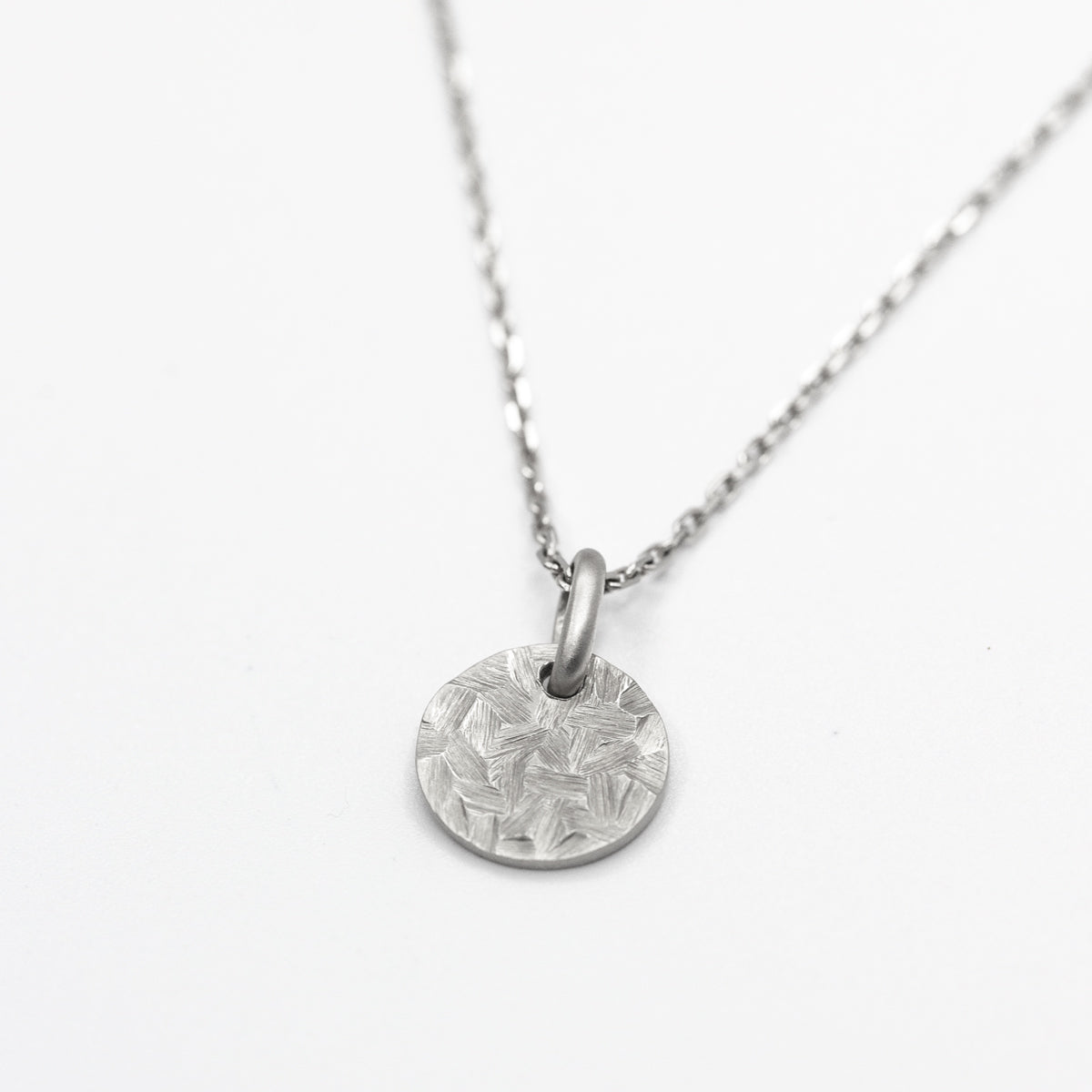 Médaille ronde de 10mm pour femme en or blanc 750/1000 martelé artisanalement dans notre atelier de joaillerie éthique. Bijou à offrir pour les baptêmes, naissances, anniversaires
