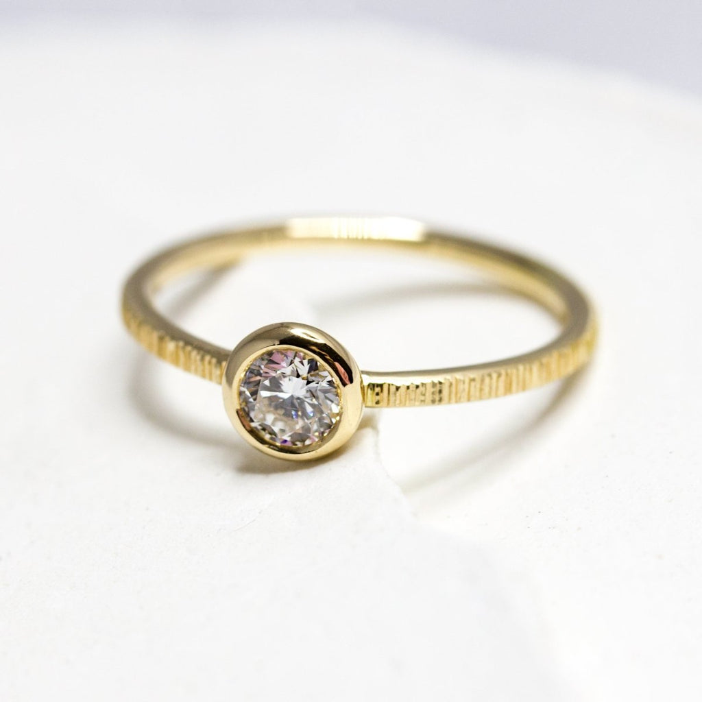 Bague de fiançailles en or jaune. L'anneau est texturé et orné d'un diamant.