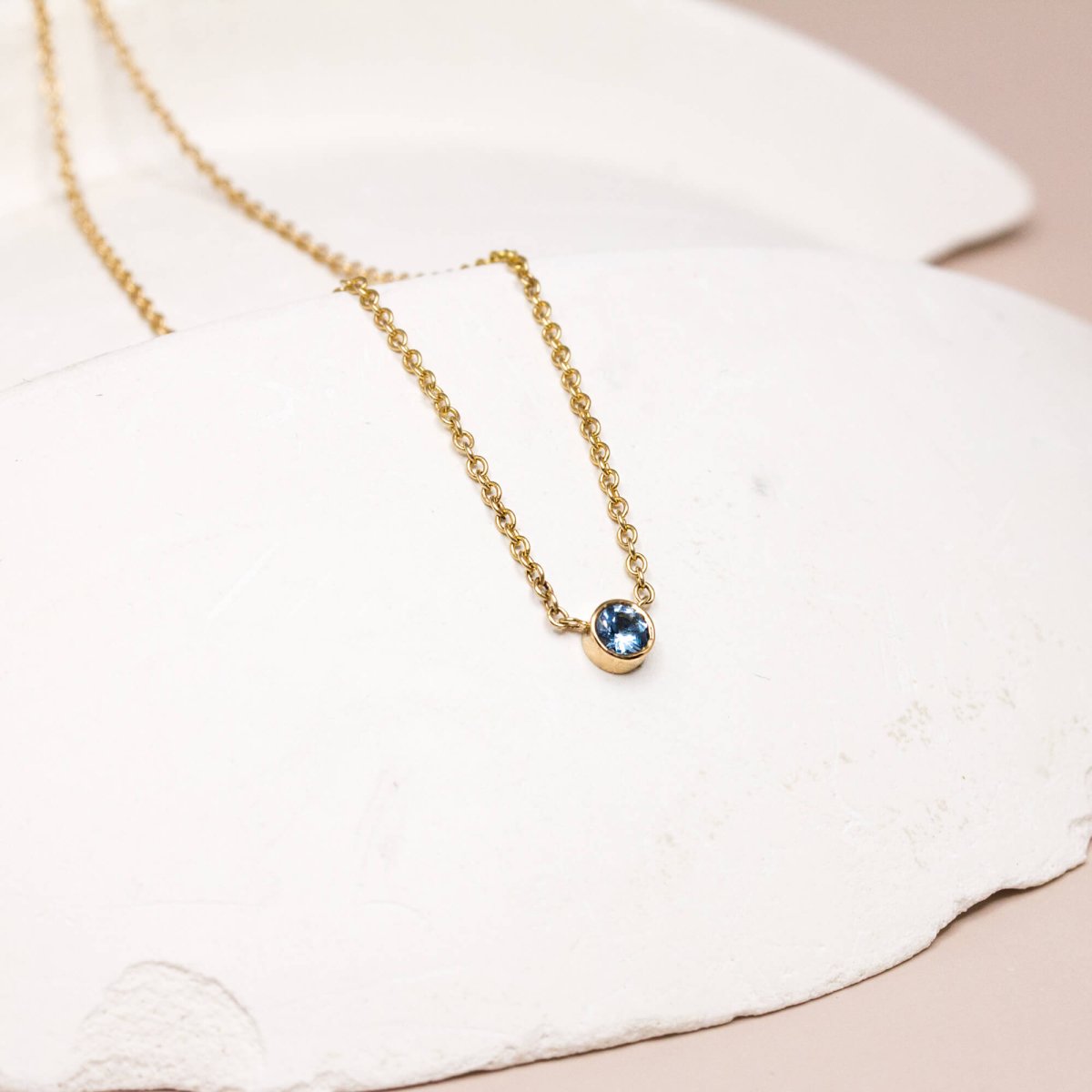 Collier unique en or équitable 18 carats orné d'une pierre bleue centrale.